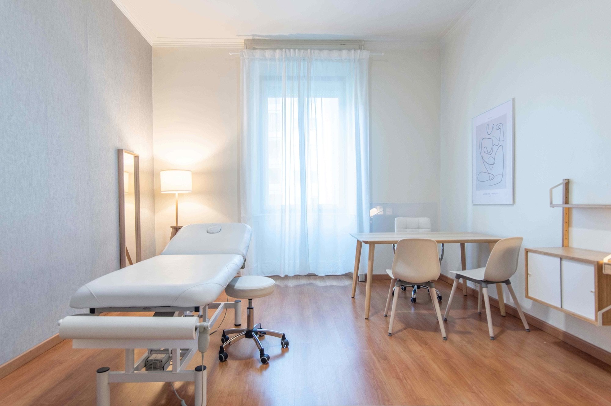 Lettino da visita con tavolo e sedute vicino alla finestra in studio olistico Exclusive presso Spatium Caiazzo, Milano