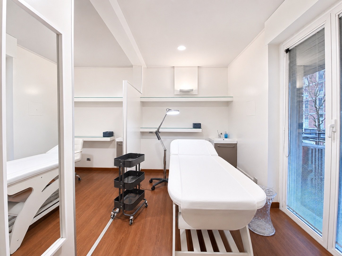 Lettino da visita con porta finestra e scrivania sullo sfondo in studio olistico Exclusive presso Spatium Triante, Monza