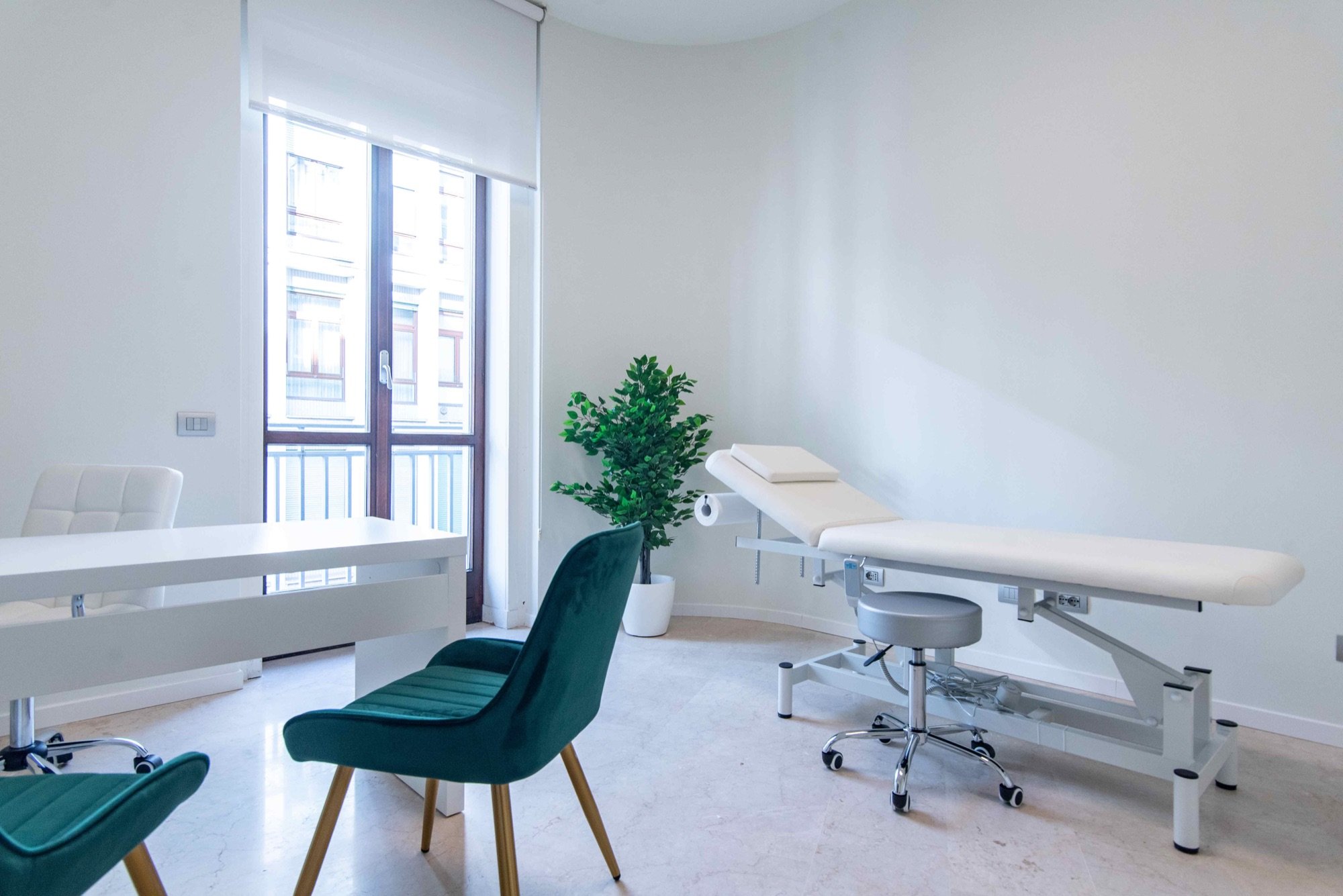 Lettino da visita vicino alla finestra con sedia verde in studio professionale Lounge presso Spatium Duomo, Milano