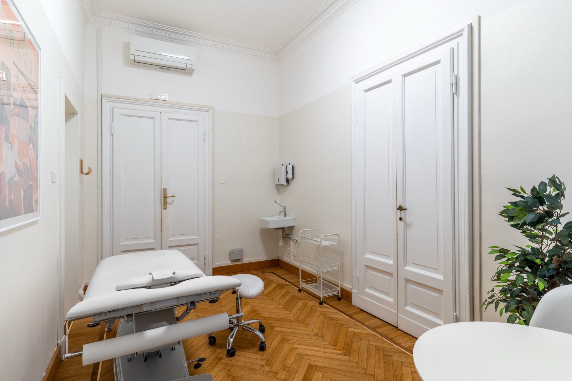 Lettino da visita con lavabo, armadio e pianta in studio professionale Premium presso Spatium Palestro, Milano