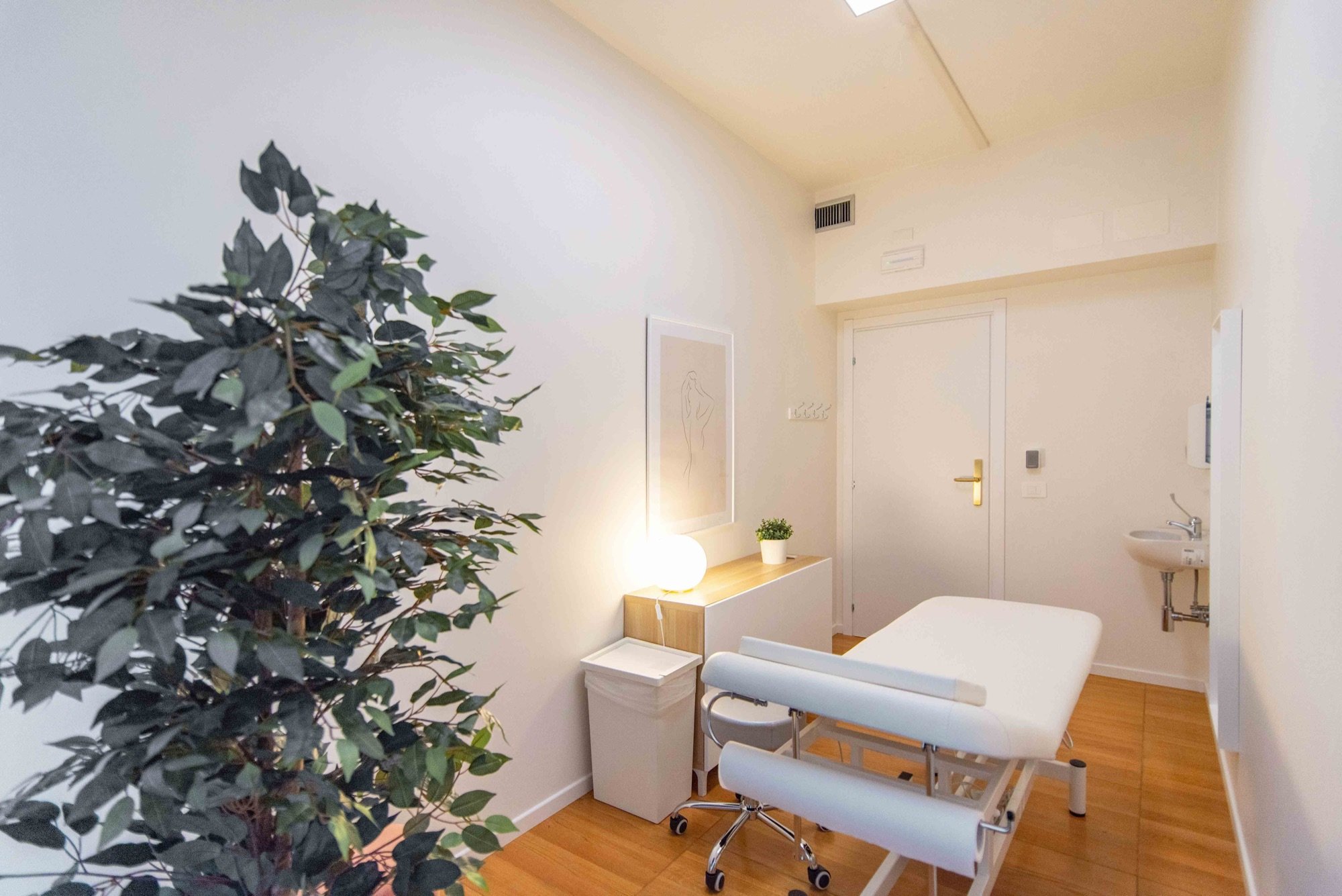 Lettino da visita con pianta e lavabo sullo sfondo in studio professionale Standard presso Spatium Corso Italia, Milano