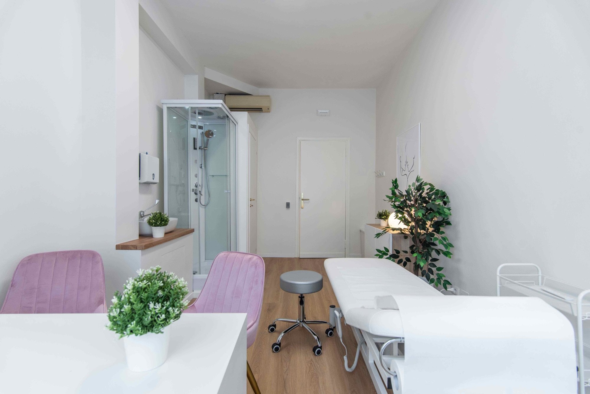 Lettino da visita con poltroncine rosa, doccia e pianta in studio professionale Exclusive presso Spatium Vittor Pisani, Milano