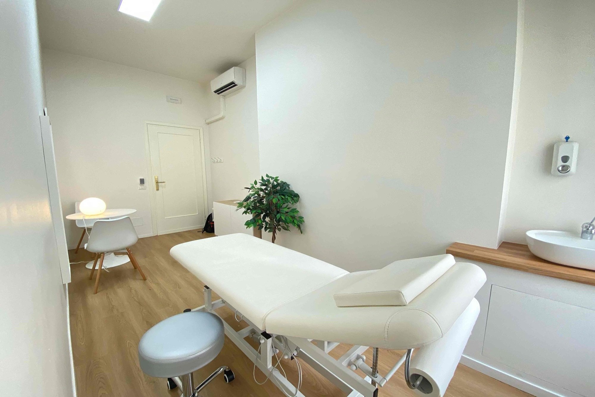 Lettino da visita con sgabello, lavabo e pianta in studio professionale Premium presso Spatium Vittor Pisani, Milano