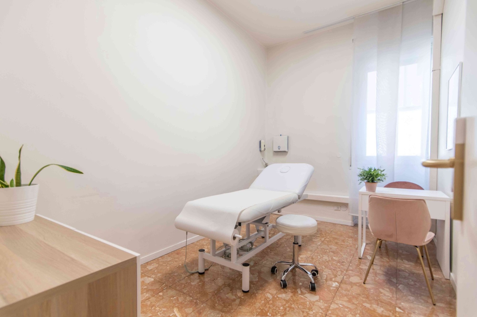 Lettino da visita con sgabello e scrivania vicino alla finestra in studio professionale Premium presso Spatium Repubblica, Milano