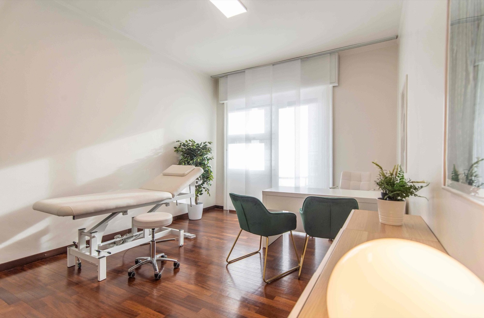 Lettino da visita con tavolo e poltroncine verdi vicino alla finestra in studio professionale Lounge presso Spatium Duomo, Milano