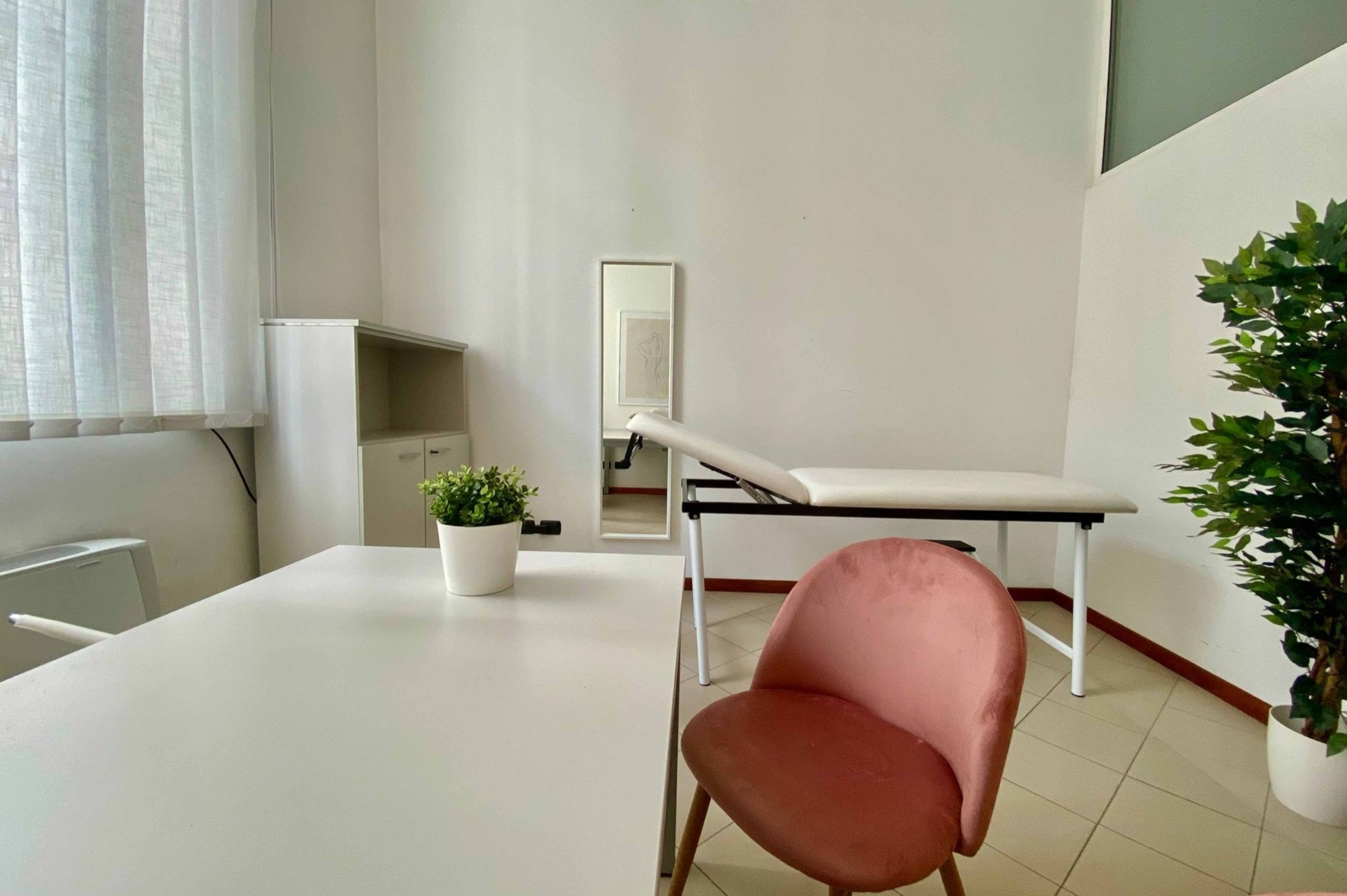 Scrivania in primo piano con poltroncina rosa e lettino sullo sfondo in studio professionale presso Spatium San Giacomo, Vigevano